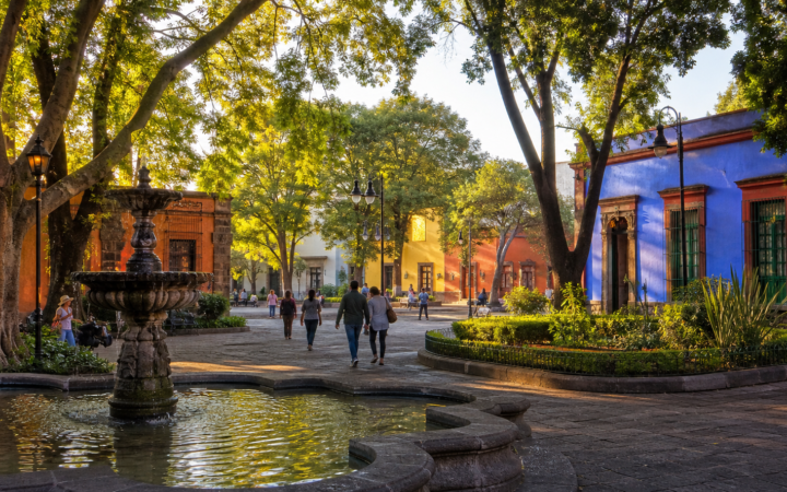 Plaza arbolada de Coyoacán con fuente y arquitectura histórica al amanecer